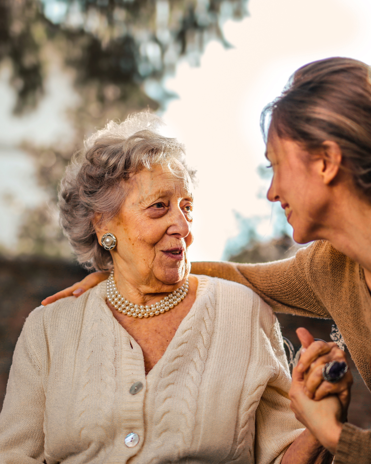 A caregiver smiling warmly with an elderly woman outdoors